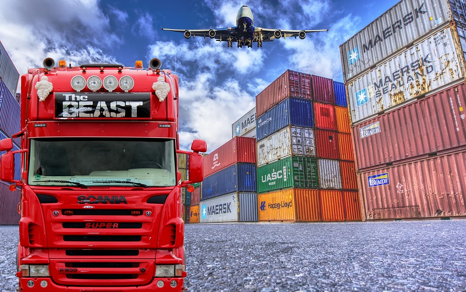 Red semi-truck with plane flying over top and storage units to the right side. 